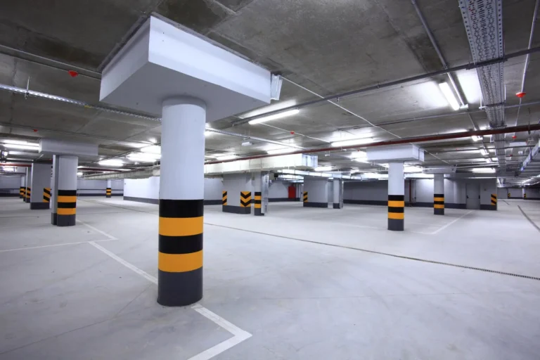 A spacious, empty underground parking garage with concrete pillars marked with black and yellow stripes, illuminated by bright overhead lights.