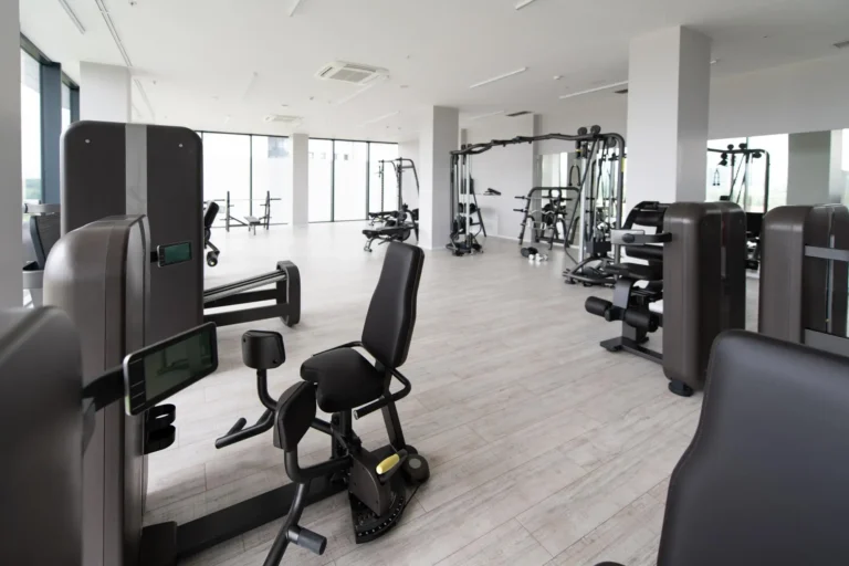 A modern gym interior featuring various exercise machines, large windows for natural light, and a spacious, clean layout.